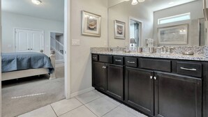 A modern bathroom with dark cabinetry, a granite countertop, and a large mirror. - Cozy home with private pool (8809) (Kissimmee)