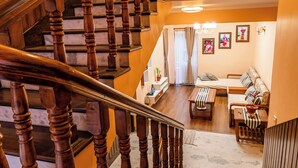 A wooden staircase with a handrail leading to a living area with a sofa, a coffee table, and a window with curtains. - Panas UK BNB (Kathmandu)