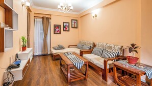 A living room with a sofa, a coffee table, a TV stand, and a chandelier. - Panas UK BNB (Kathmandu)