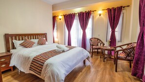 A bedroom with a wooden bed, a bedside table, a chair, and a small table with a vase. - Panas UK BNB (Kathmandu)