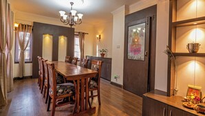 A dining area with a wooden table and chairs, a chandelier, and a kitchen area with a stove and cabinets. - Panas UK BNB (Kathmandu)