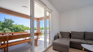 Un salon moderne comprenant un canapé, une petite table et une porte-fenêtre coulissante donnant sur une terrasse extérieure avec un banc en bois et une table.