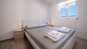 Une chambre à coucher minimaliste, avec un lit simple, des tables de chevet, une fenêtre donnant sur un paysage et une porte.