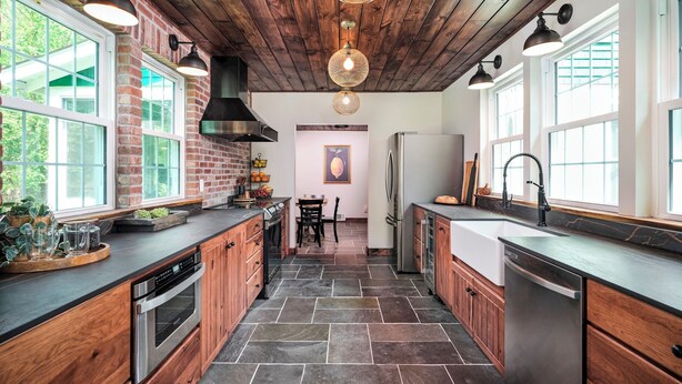Una cucina moderna con mobili in legno, pavimento in pietra e ampie finestre.