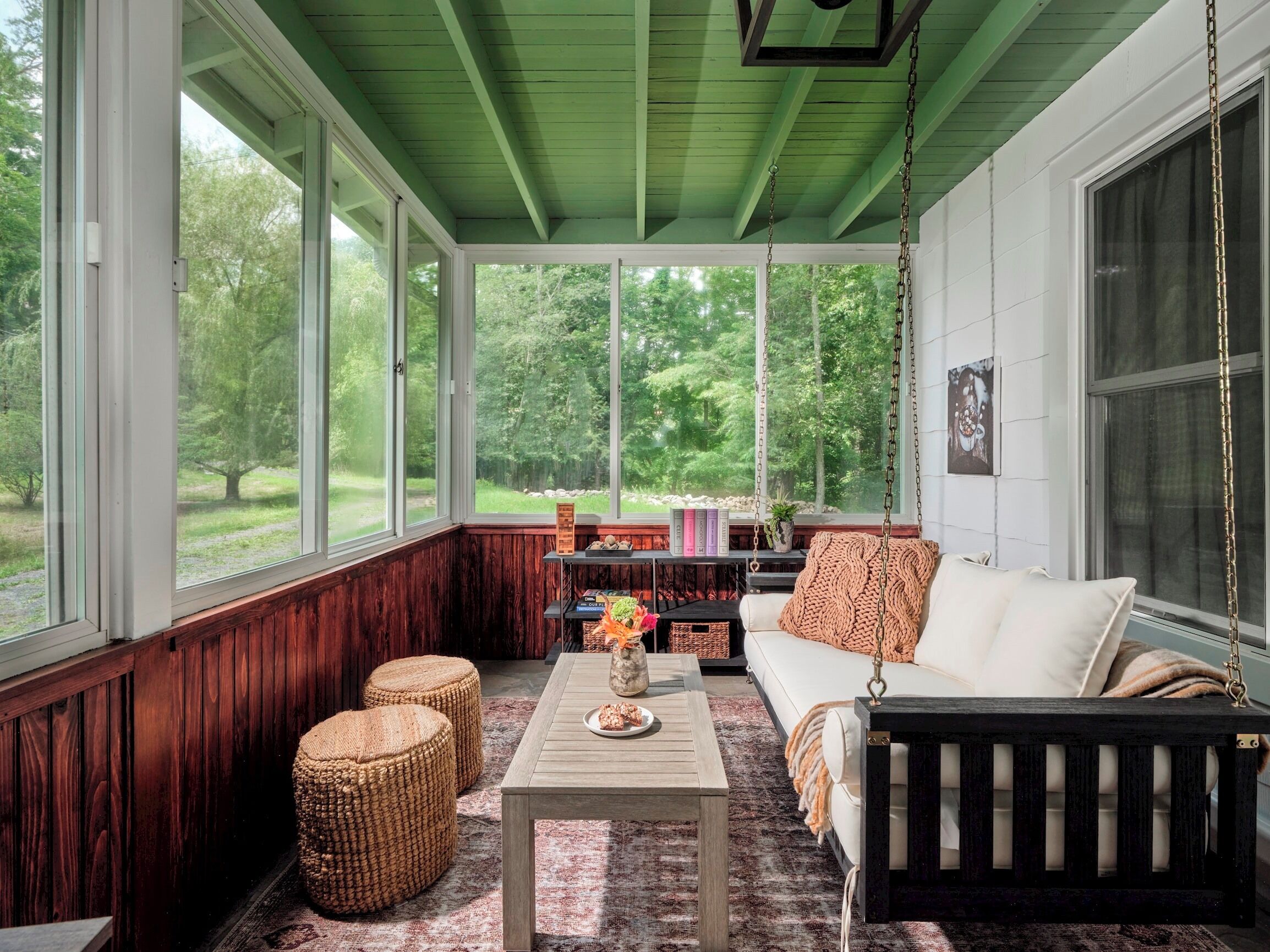 A cozy room with a green ceiling, large windows, a white sofa, a wooden coffee table, and wicker ottomans.