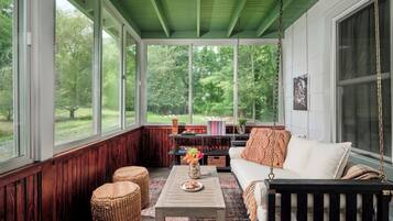 A cozy room with a green ceiling, large windows, a white sofa, a wooden coffee table, and wicker ottomans.