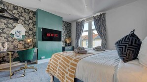 A hotel room with a bed, a desk, a TV, and a window with curtains. - 3BR Chic House withParking Sleeps 8, Big Groups! (Portsmouth)