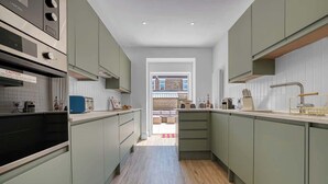 A modern kitchen with light green cabinets, a built-in oven, and a view to an outdoor seating area. - 3BR Chic House withParking Sleeps 8, Big Groups! (Portsmouth)