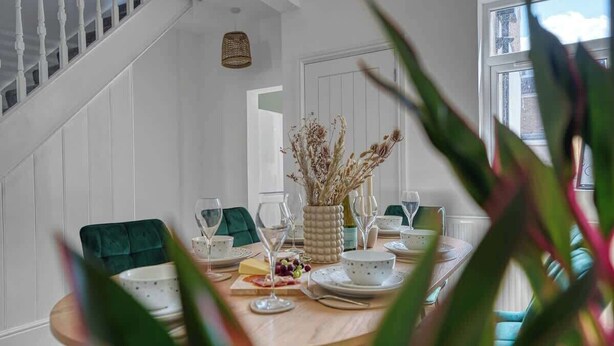 A dining area with a wooden table set for four, white walls, a staircase, and a window. - 3BR Chic House withParking Sleeps 8, Big Groups! (Portsmouth)