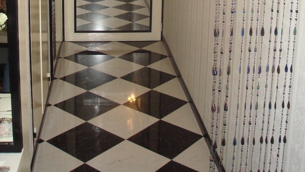 Un pasillo con piso de cuadros, una puerta al final y cortinas de cuentas decorativas en la pared derecha.