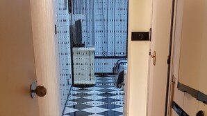 Un pasillo con piso a cuadros blanco y negro que conduce a una habitación con cortina azul y pared estampada.