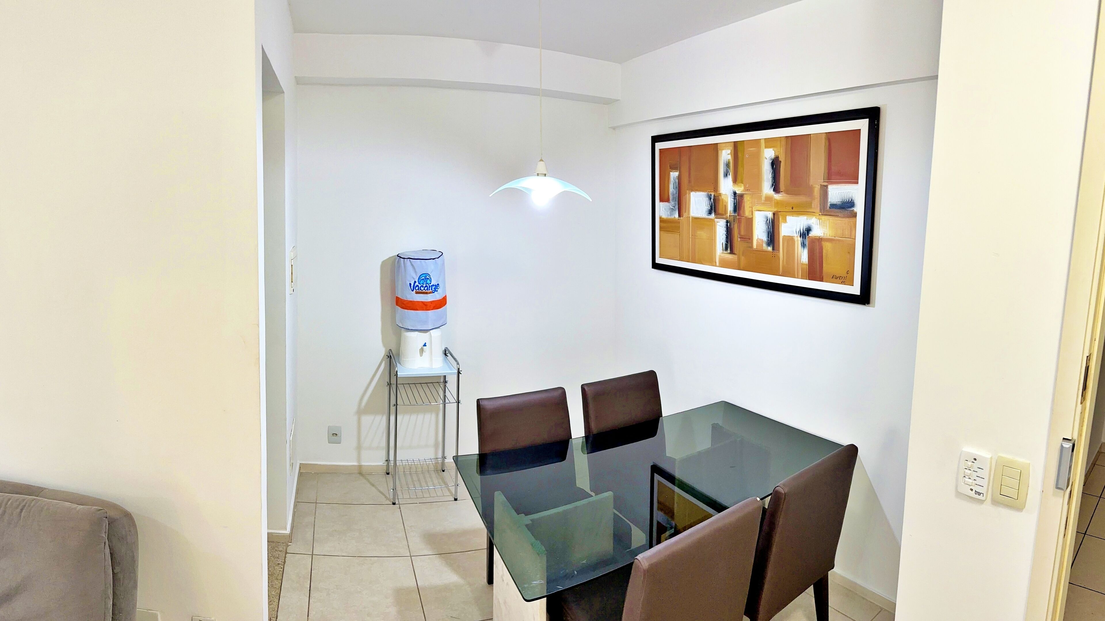 A dining area with a glass table and brown chairs, a water dispenser, and a framed artwork on the wall.