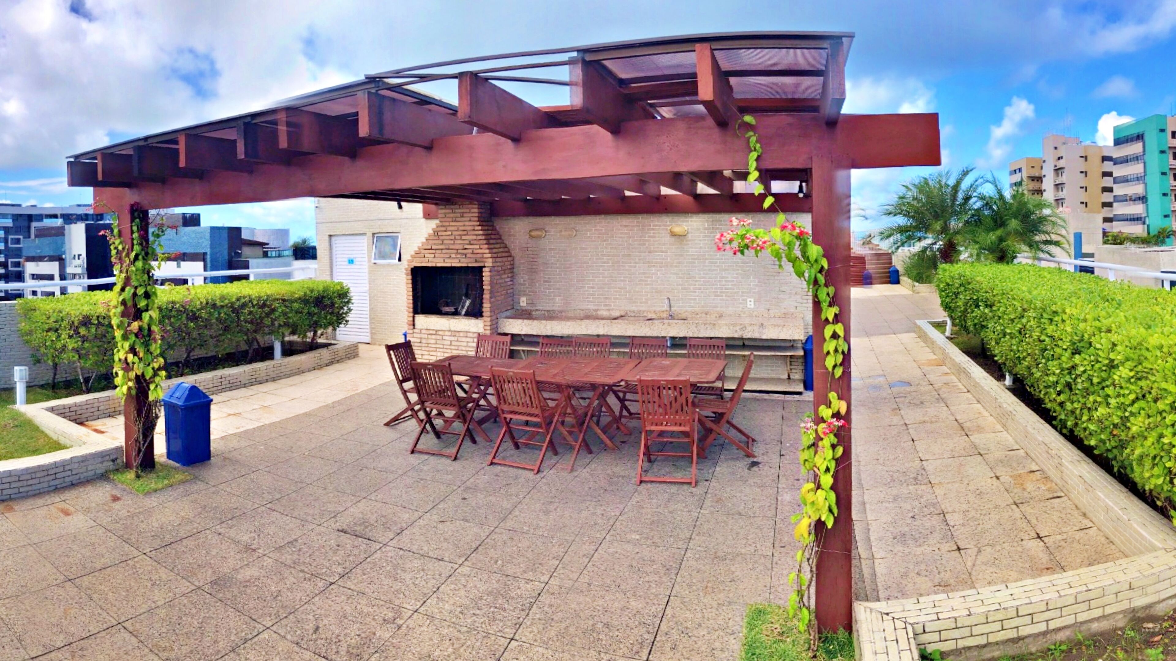 Un patio al aire libre con una parrilla de ladrillo, mesas y sillas de madera, y una estructura de pérgola.