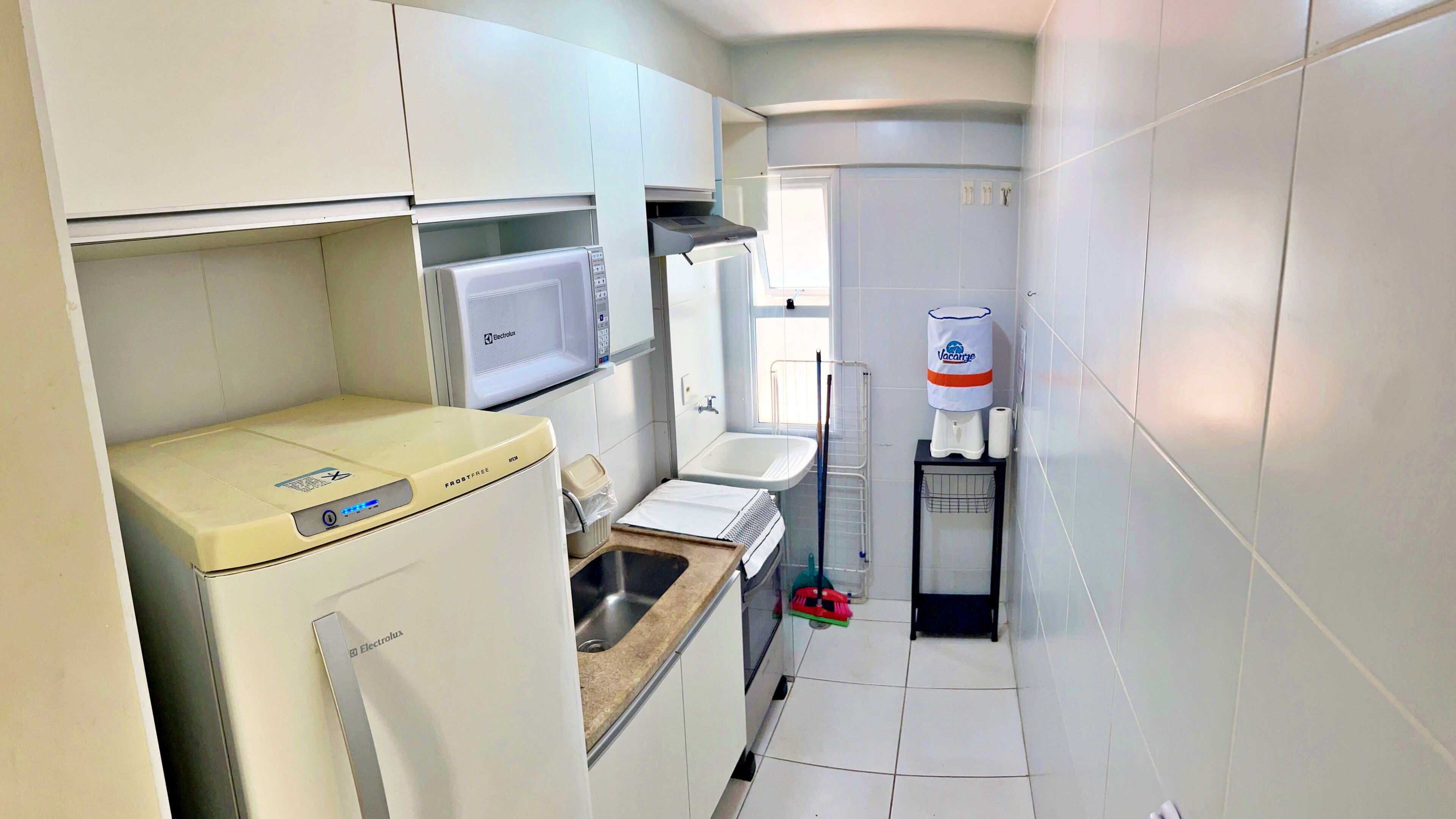 A compact kitchen with a refrigerator, microwave, sink, and a water dispenser.