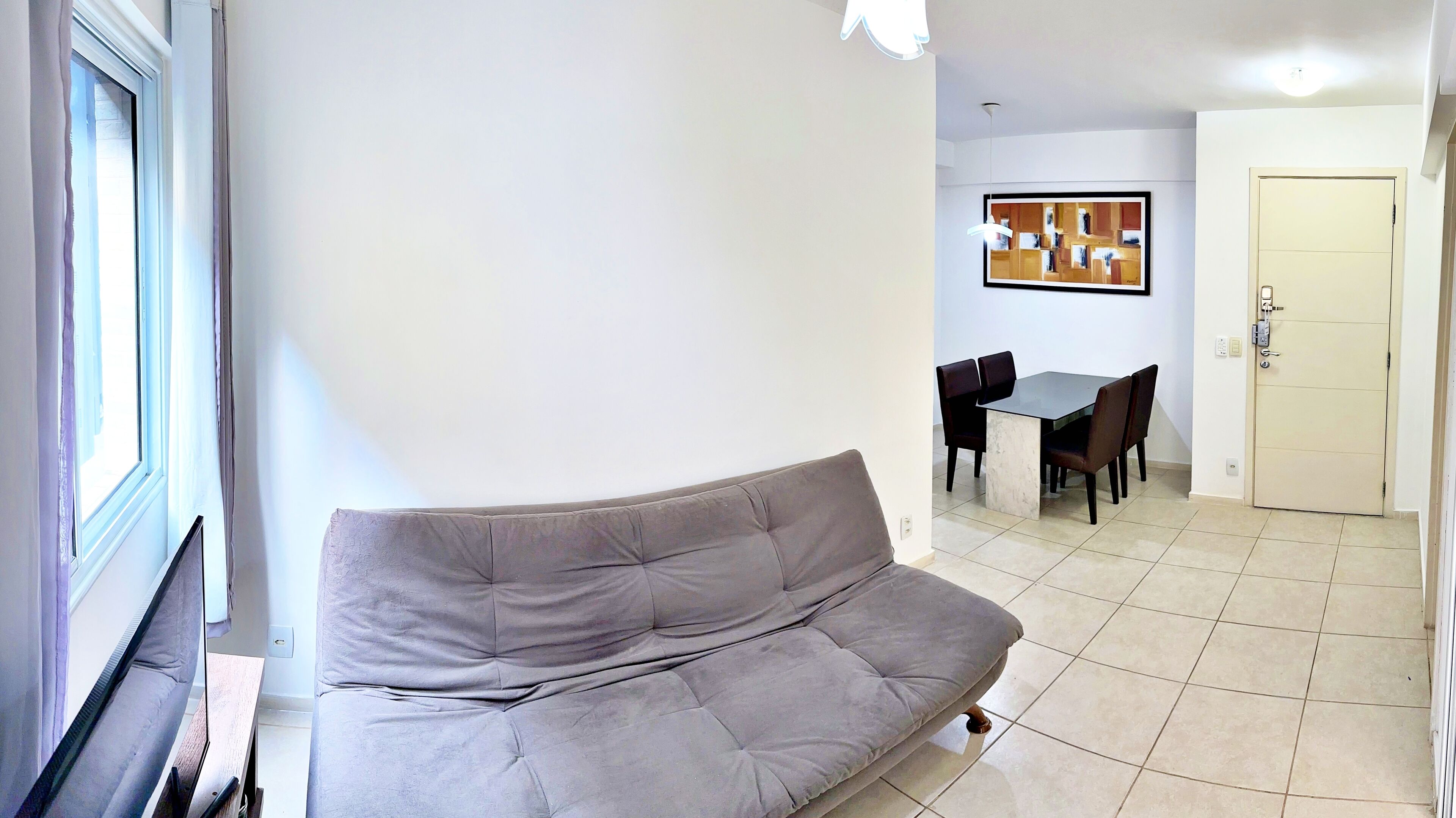 Una sala de estar con un sofá gris, una mesa de comedor con sillas y una puerta.
