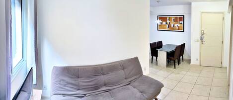 A living room with a grey sofa, a dining table with chairs, and a door.