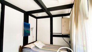 Ein kleines Zimmer mit einem Bett, einem Sessel, einem Bild an der Wand und einem Fenster mit Vorhängen.