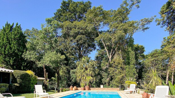 Ein rechteckiger Swimmingpool mit gefliesten Rändern, umgeben von Steinplatten und weißen Liegestühlen.