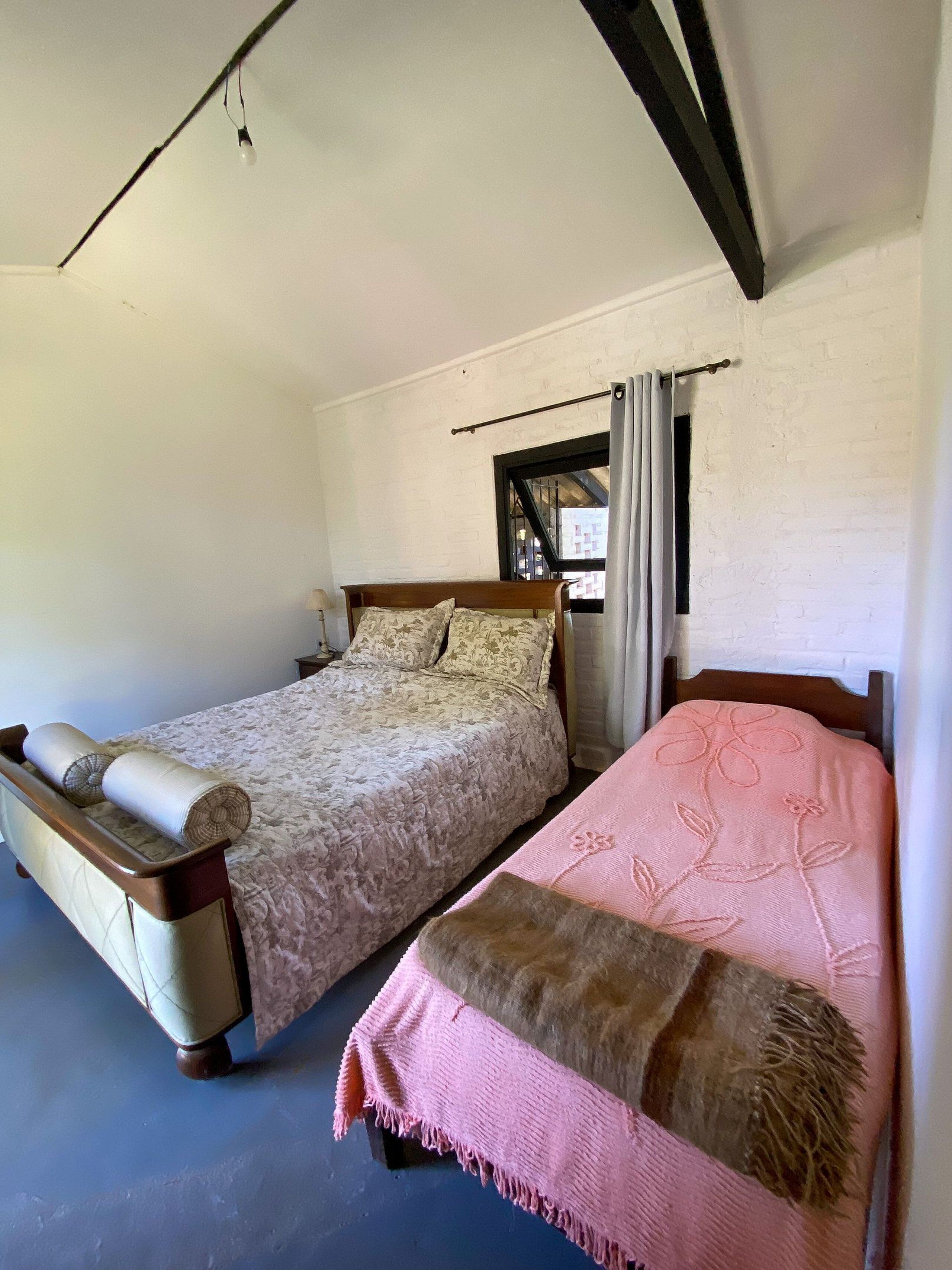 A room with two beds, a window with curtains, and a wooden ceiling beam.