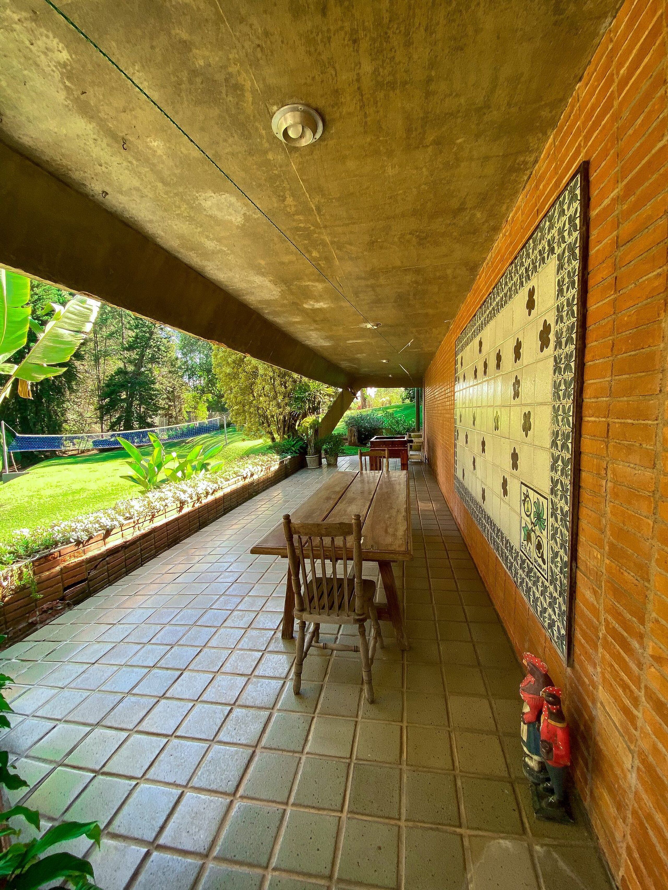 Une terrasse extérieure couverte, dotée d’un sol carrelé, d’une table en bois et de chaises.