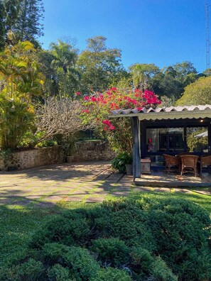 A covered outdoor seating area with a stone wall and lush greenery. - Chácara Espetacular em Ibiúna (Ibiuna)