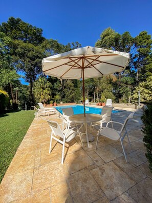 Una piscina con borde de baldosas, rodeada de sillas de descanso blancas y una mesa con sombrilla.