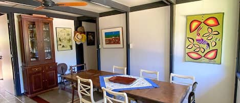 A dining area with a wooden table, white chairs, a patterned rug, and artwork on the walls.