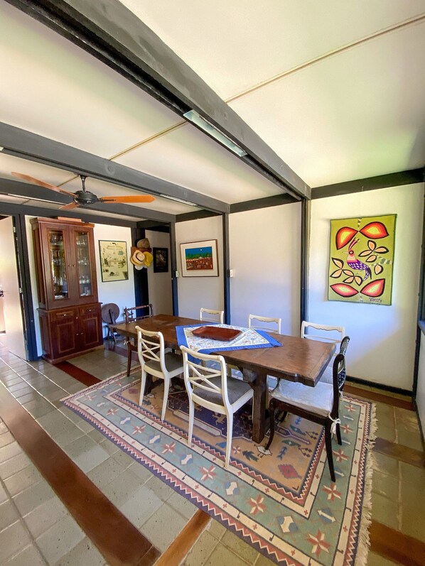 Un comedor con una mesa de madera, sillas blancas, un tapete estampado y obras de arte en las paredes.