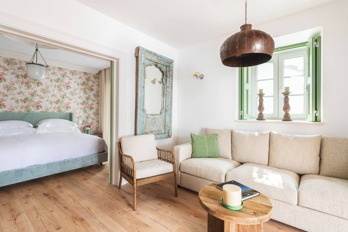 A room with a bed, a wicker chair, a sofa, a wooden coffee table, and a mirror on the wall.