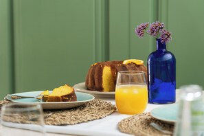 Un desayuno con pastel, un vaso de jugo de naranja y un florero con flores.
