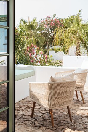 Wicker chairs with cushions on a stone patio with a view of a garden with pink flowers and palm trees. - The Green House by Santiago de Alfama (Alvito)