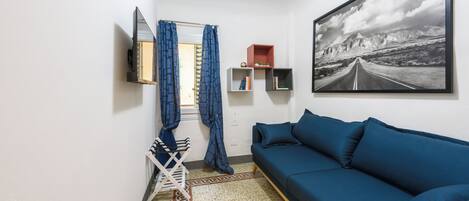 A room with a blue sofa, a mounted TV, a framed picture, and a window with curtains.