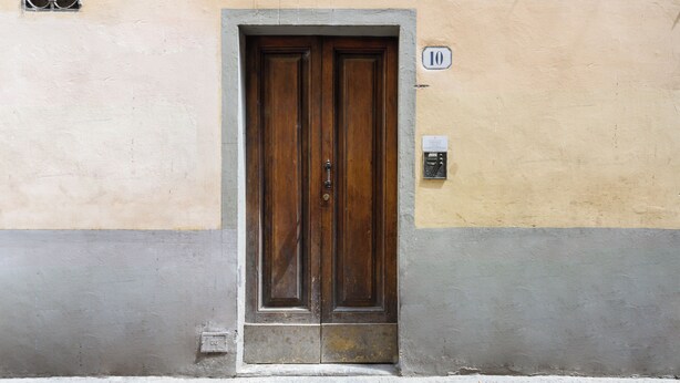 A wooden double door with a metal handle, set in a building with a beige and gray facade. - Osteria del Guanto by Mmega (Florence)