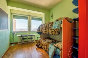 Een studentenkamer met stapelbedden, een bureau, stoelen en een raam met uitzicht.