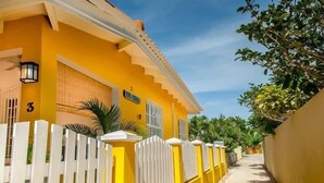 A yellow building with a white fence, a sign reading "Faz Koron," and a number "3" on the wall. - 03 Kas Koral by Bonaire Paradise (Kralendijk)
