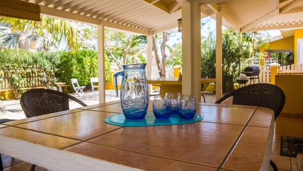 A covered outdoor dining area with a table set for two, surrounded by chairs, a pitcher, and glasses. - 03 Kas Koral by Bonaire Paradise (Kralendijk)