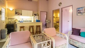 A cozy living room with pink furniture, a glass coffee table, and a kitchen in the background. - 03 Kas Koral by Bonaire Paradise (Kralendijk)