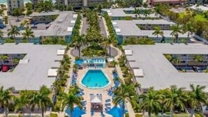 Un complexe hôtelier doté d’une piscine centrale, entourée de palmiers et de chaises longues.