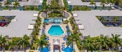 A resort with a central swimming pool, surrounded by palm trees and lounge chairs.