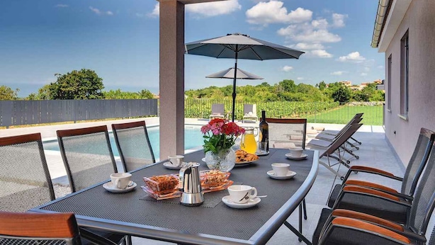 Un espace extérieur aménagé pour prendre les repas, avec une table dressée pour le petit-déjeuner, des chaises et des parasols.