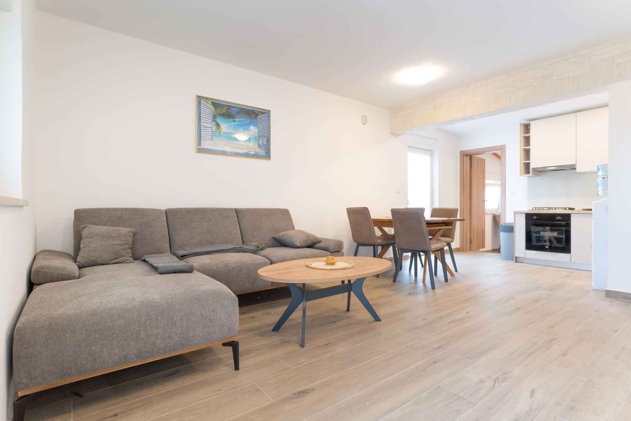 Ein modernes Wohnzimmer mit einem grauen Sofa, einem runden Couchtisch und einem Essbereich mit Stühlen und Tisch.