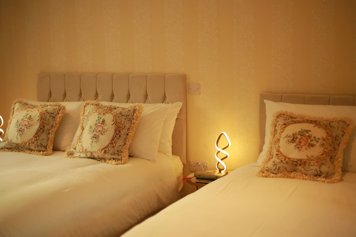 Two beds with floral-patterned pillows and a nightstand with a lamp.