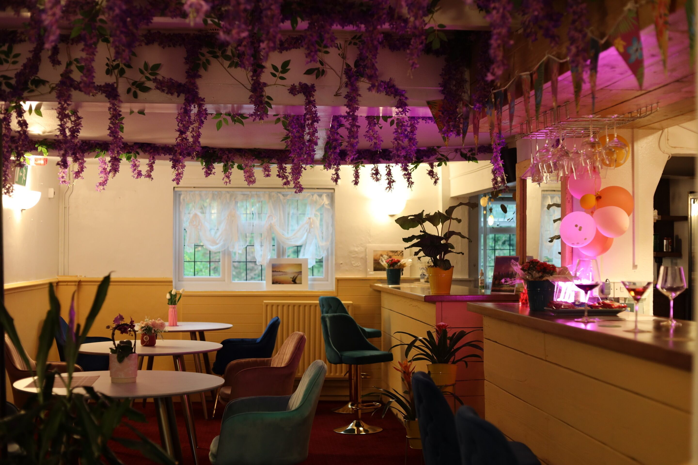 A cozy dining area with round tables, colorful chairs, and hanging purple flowers.