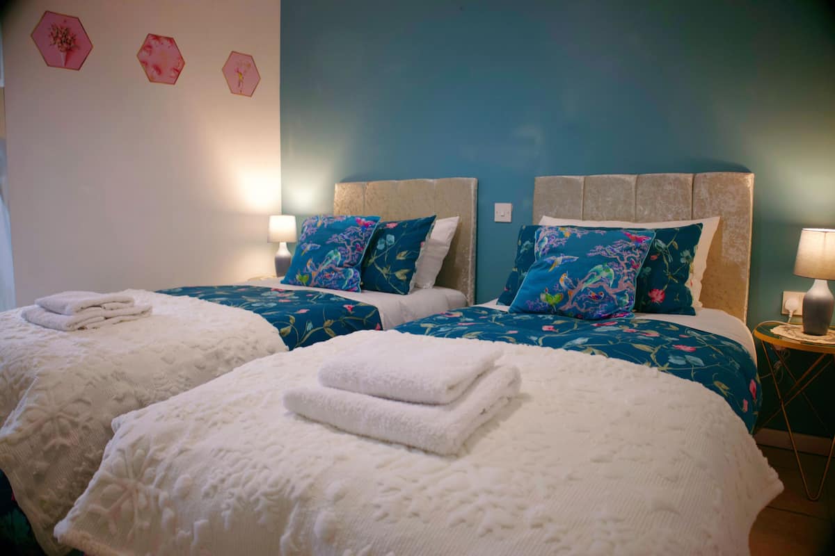 A hotel room with two beds, each with a floral bedspread and matching pillows. There are folded towels on each bed.