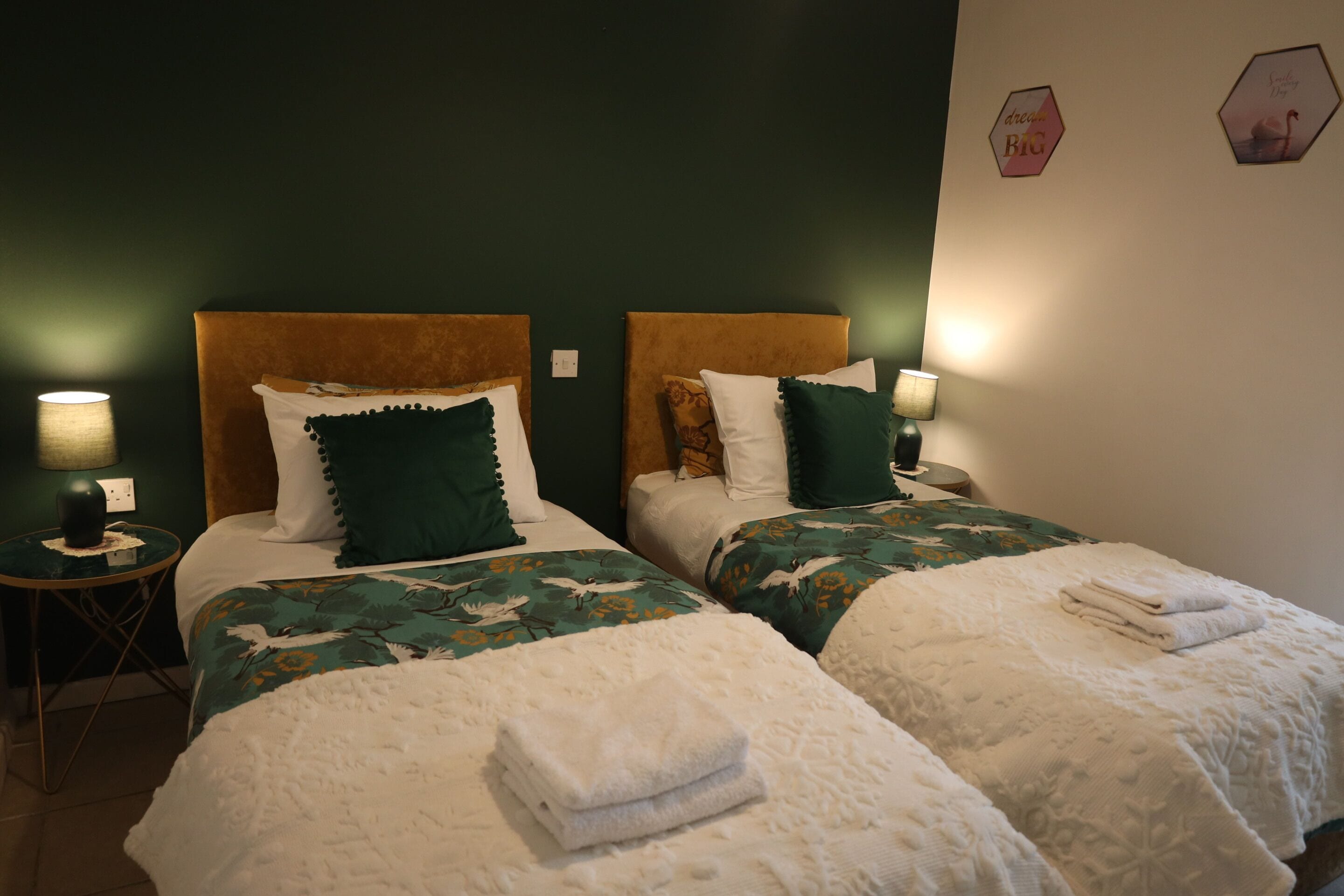 Habitación de hotel con dos camas, cada una con cabecero, mesitas de noche, lámparas y cojines decorativos.