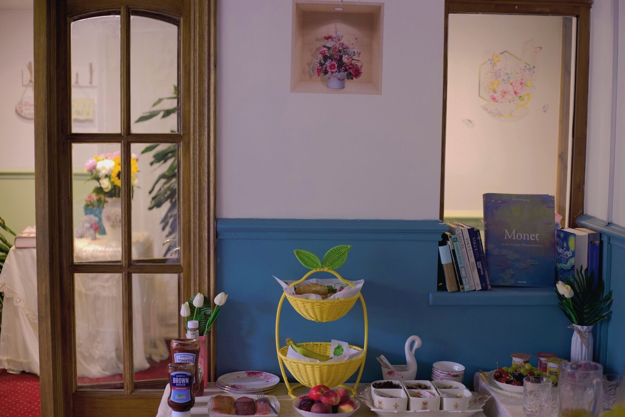A dining table with a bottle of brown sauce, a plate of fruits, and a basket of bread.