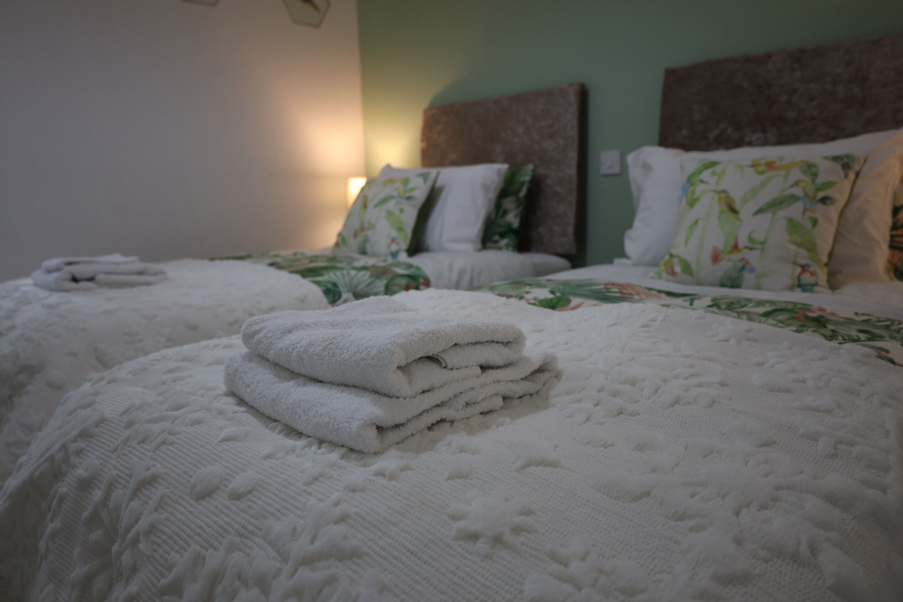 A hotel room with two beds, each with a white quilt and pillows with a tropical print.