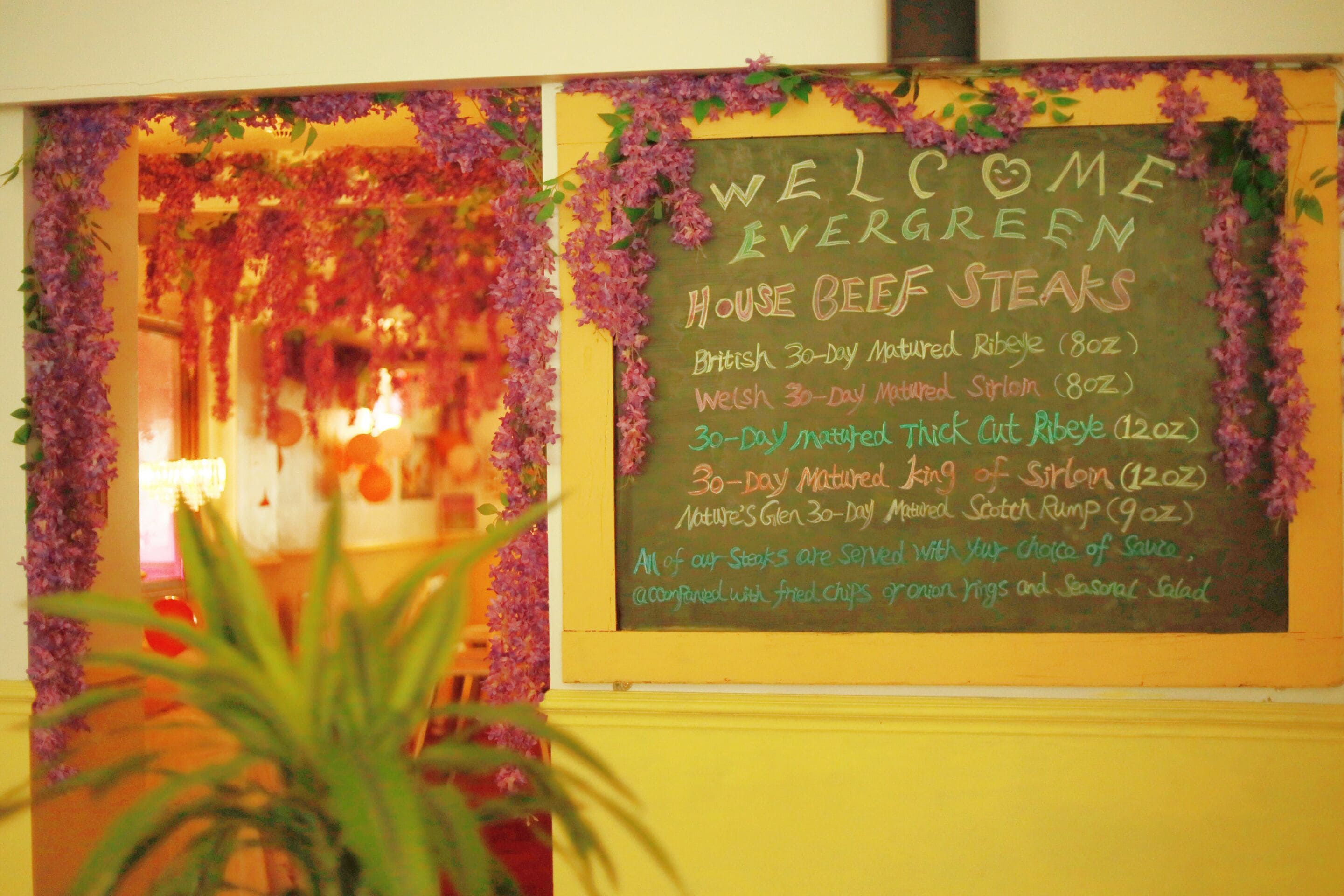 Eine Kreidetafel mit verschiedenen Rindfleisch-Steak-Angeboten und einer dekorativen Blumenkomposition.