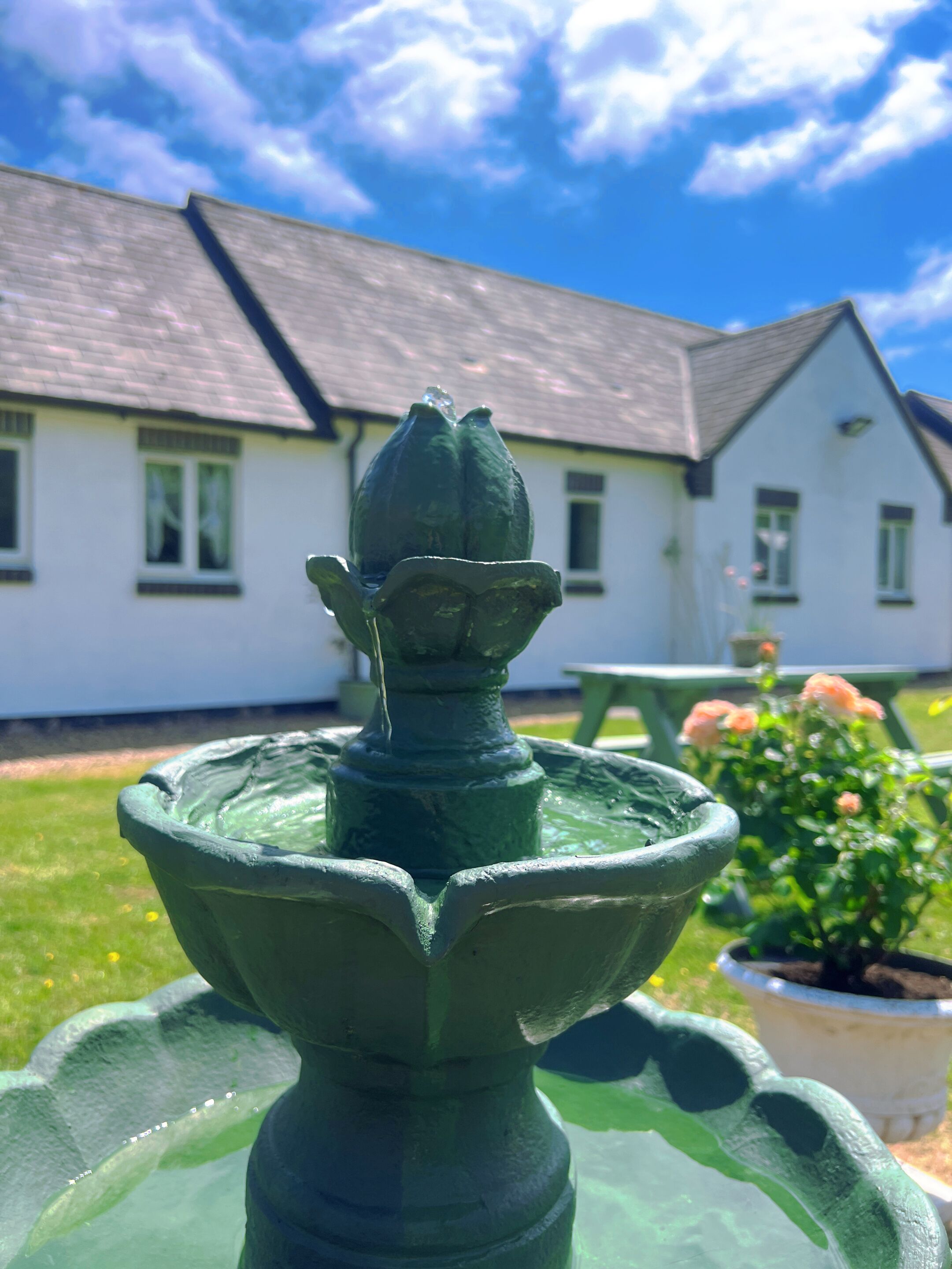 Een groene buitenfontein met een huis op de achtergrond.