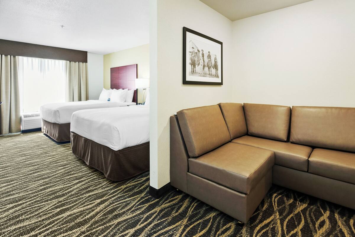A hotel room with two beds, a brown leather sofa, a patterned carpet, and a framed picture on the wall.